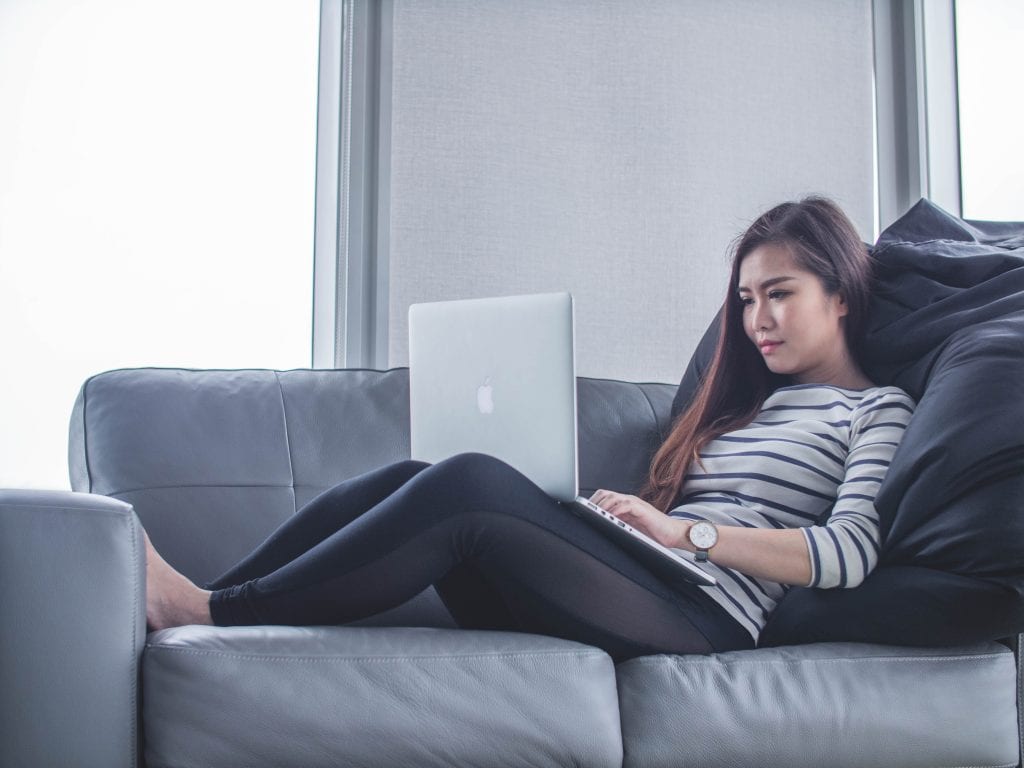 Woman laying on sofa with laptop working at home 
