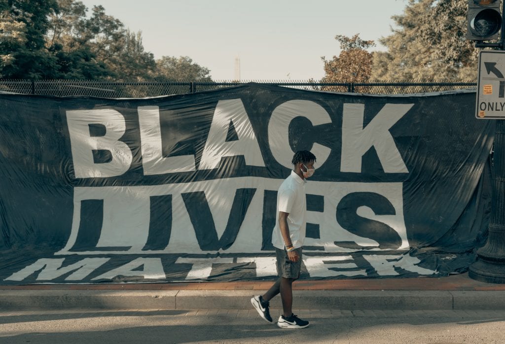 Man walks in front of a Black Lives Matter flag (IG: @clay.banks)